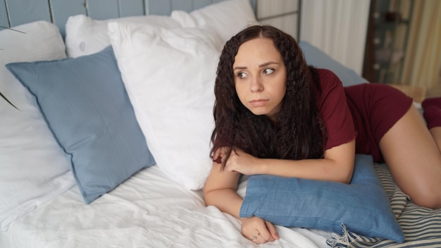 Retrato de joven mujer bonita en pijama acostada en la cama abrazada con almohada en la mañana Primer plano de una dama adulta descansando y mirando soñadoramente lejos