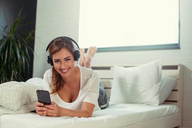 Retrato de una joven mujer casual con auriculares escuchando música en pijama