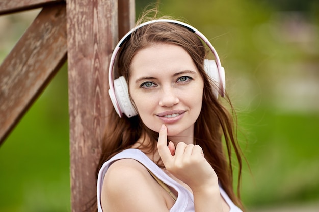 Retrato de joven mujer caucásica en auriculares inalámbricos en el parque