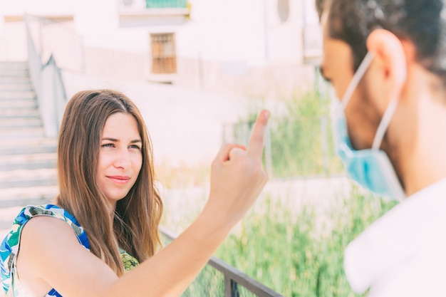 Retrato de una joven mujer caucásica mostrando su dedo medio a un joven con una máscara