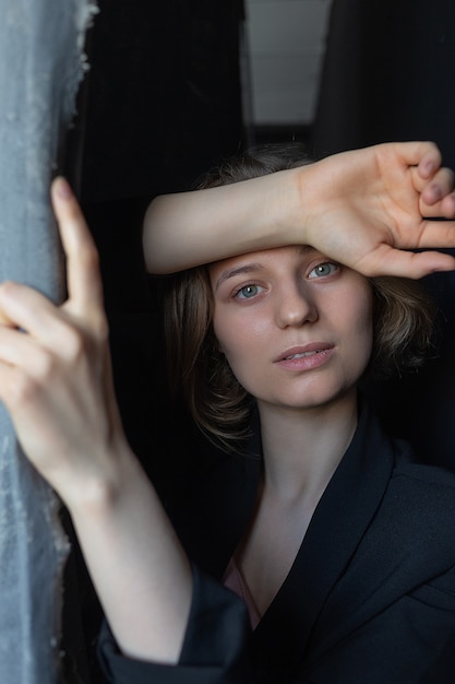 Retrato de joven mujer caucásica con pelo corto posando en traje negro chaqueta, sosteniendo la cortina. tiro del primer de la muchacha bonita. poses femeninas atractivas de pelo corto en estudio