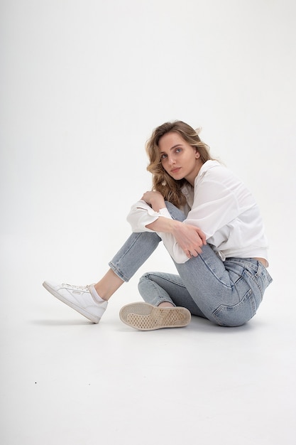 Retrato de joven mujer caucásica pensativa posando en camisa y pantalones vaqueros azules