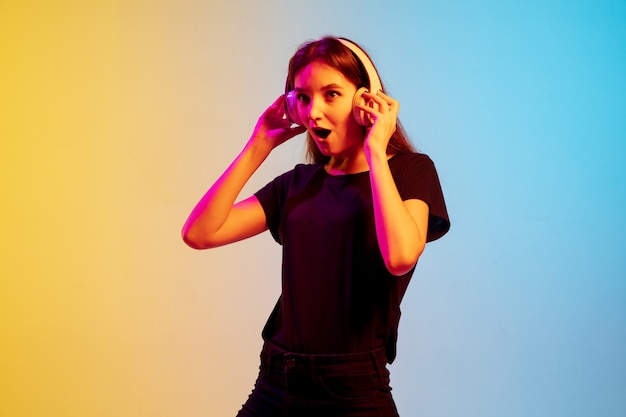 Retrato de joven mujer caucásica sobre fondo de estudio azul-amarillo degradado en luz de neón