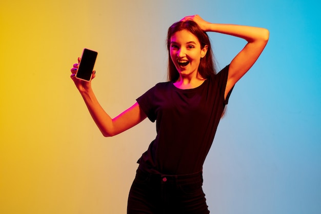 Retrato de joven mujer caucásica sobre fondo de estudio azul-amarillo degradado en luz de neón