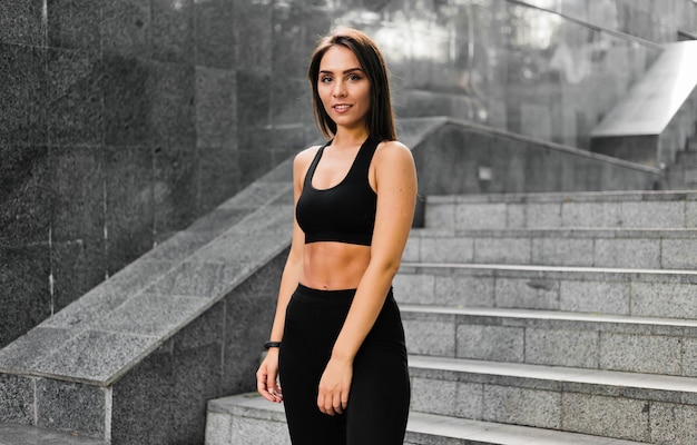 Retrato de joven mujer deportiva bronceada en escaleras de mármol gris al aire libre