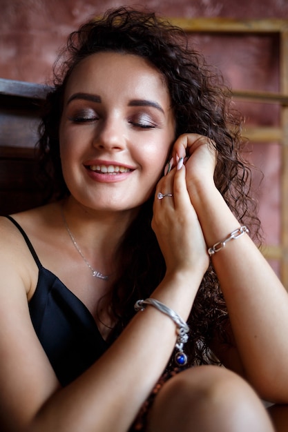 Retrato de una joven mujer encantadora con cabello rizado, chica de piel clara en un top negro y con una sonrisa en su rostro