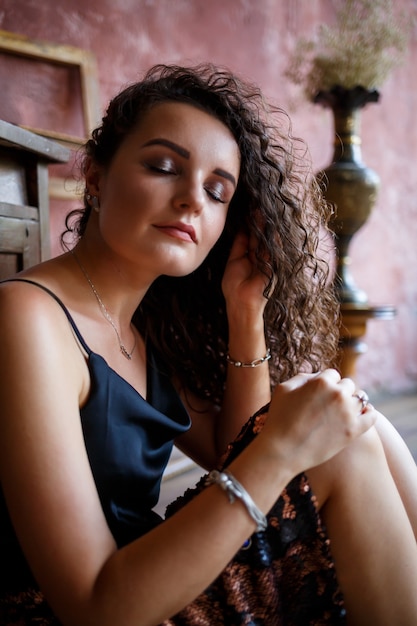 Retrato de una joven mujer encantadora con cabello rizado, chica de piel clara en un top negro y con una sonrisa en su rostro