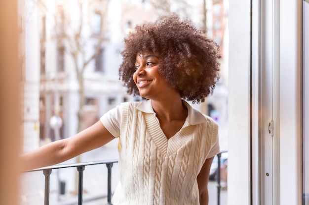 Retrato de una joven mujer étnica negra con cabello afro en un balcón en casa sonriendo situación cotidiana al atardecer