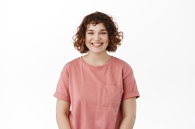 Retrato de una joven mujer feliz sonriendo a la cámara, de pie en una camiseta casual contra un fondo blanco.