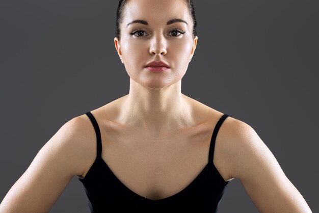 Foto retrato de una joven mujer fitness con pantalones deportivo negro, hermosa modelo segura de sí misma mirando a la cámara con fondo gris. estilo de vida deportivo saludable, gente joven, concepto de cuerpo atlético saludable