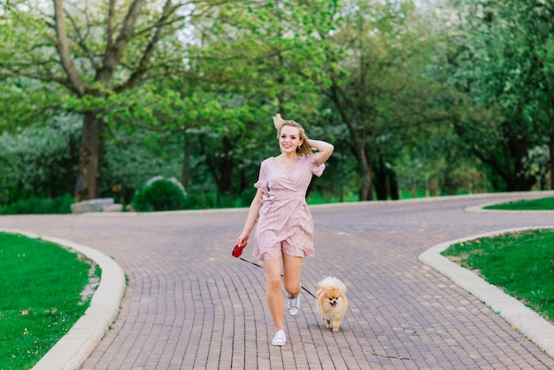 Retrato de una joven mujer glamorosa con vestido rosa sosteniendo su lindo spitz pomerania en las manos. . Concepto de amistad entre perros y humanos.