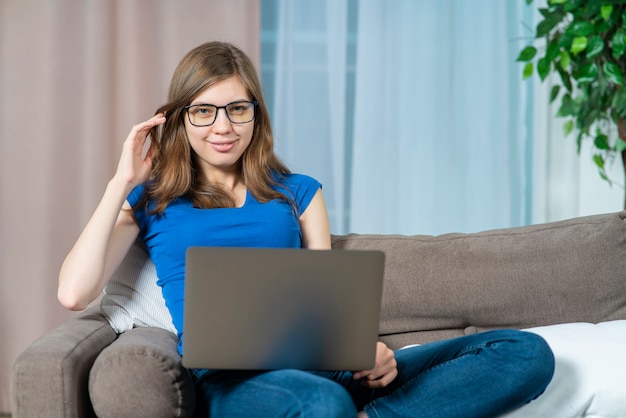 Retrato de joven mujer hermosa feliz freelancer en gafas estudiante chica sentada en casa en el sofá