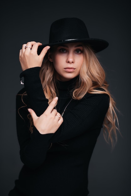 Retrato de una joven mujer hermosa con sombrero negro en la pared negra