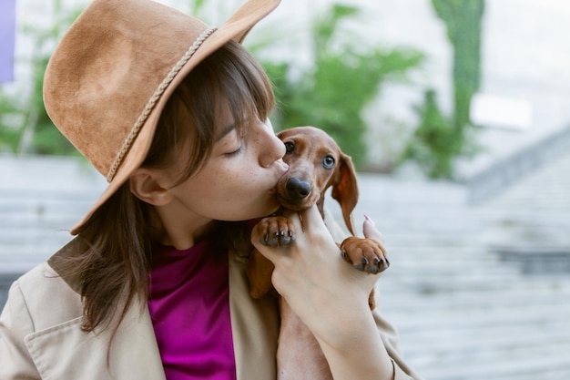 Retrato de una joven mujer de moda y un encantador cachorro dachshund en un parque de la ciudad. Ama y mascota