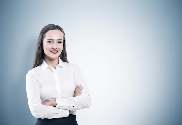 Retrato de una joven mujer de negocios alegre de pie con los brazos cruzados y mirándote. Ella lleva una blusa blanca y una falda negra.