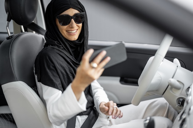 Retrato de una joven mujer de negocios musulmana con hijab habla por teléfono mientras conduce un automóvil. Concepto de globalización y modernización de la sociedad islámica y los derechos de las mujeres