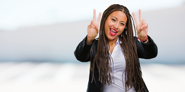 Retrato de una joven mujer de negocios negra divertida y feliz, positiva y natural, hace un gesto de victoria, concepto de paz