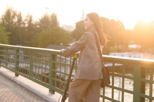 Retrato de una joven mujer de negocios con un scooter eléctrico para trabajar sobre un puente