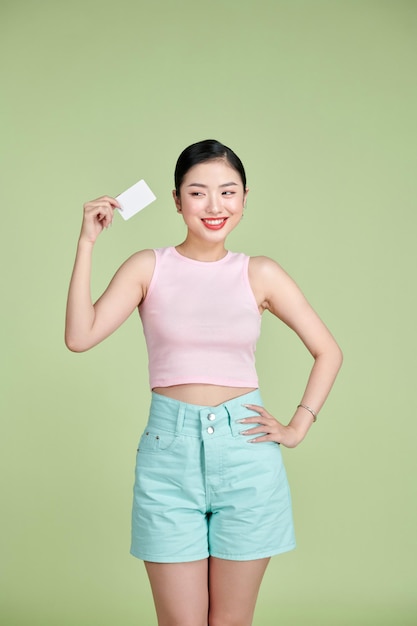 Retrato de una joven mujer de negocios sonriente sosteniendo una tarjeta de crédito vacía aislada de fondo verde