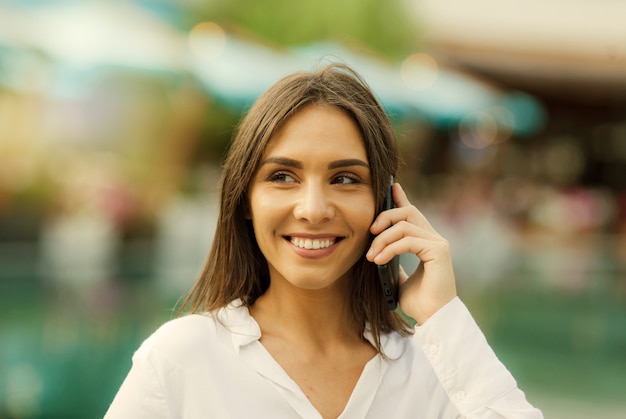 Retrato de una joven mujer de negocios vestida con una blusa blanca mientras habla por teléfono al aire libre