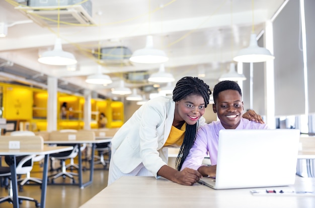 Retrato de una joven mujer negra y un chico sonriendo en un entorno de trabajo con cuadernos, empresario o estudiante africano