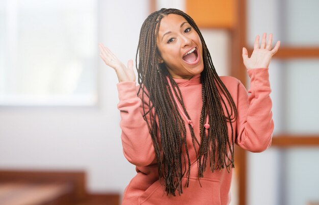 El retrato de una joven mujer negra que lleva trenzas riéndose y divirtiéndose, relajado y alegre, se siente seguro y exitoso
