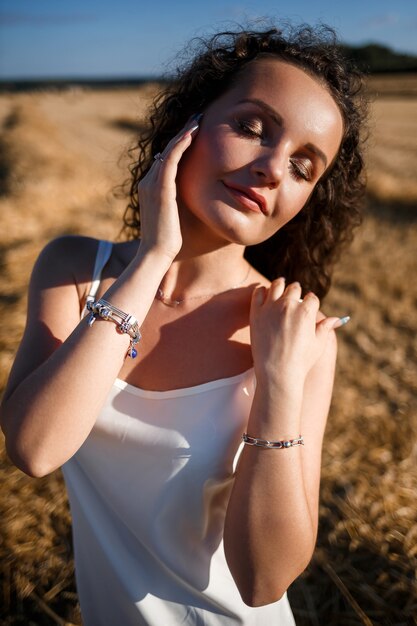 Retrato de una joven mujer rizada en un campo de trigo, donde se corta el trigo y las gavillas están de pie, disfrutando de la naturaleza. Naturaleza. rayos de sol agricultura