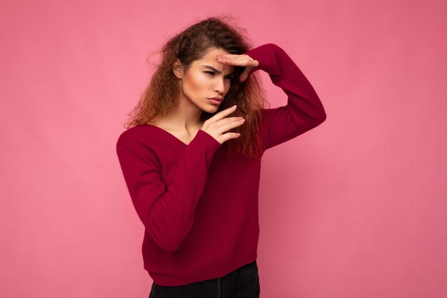 Retrato de joven mujer rizada morena hermosa seria con emociones sinceras vistiendo rosa de moda