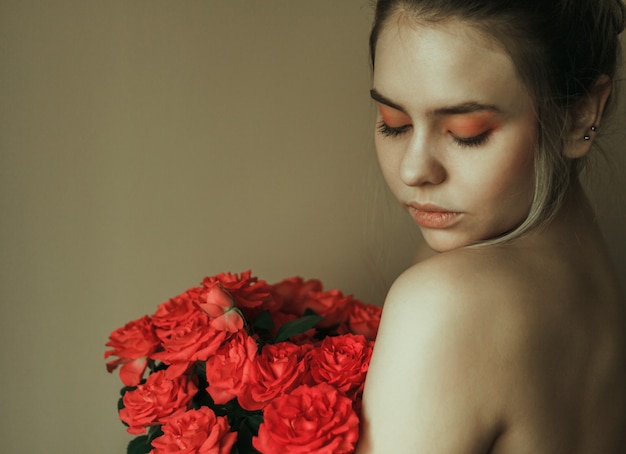 Retrato de una joven mujer rubia con maquillaje rojo y un ramo de rosas