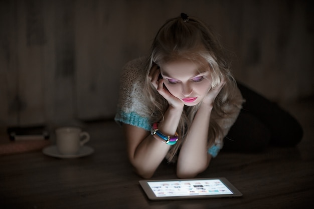 Retrato de joven mujer rubia mira y lee en la tableta y tomando café en la noche chica usa el ...