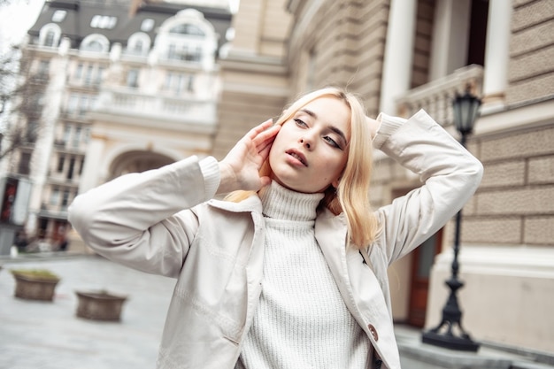 Retrato de una joven mujer rubia de moda en una gabardina de otoño contra el fondo de la arquitectura urbana