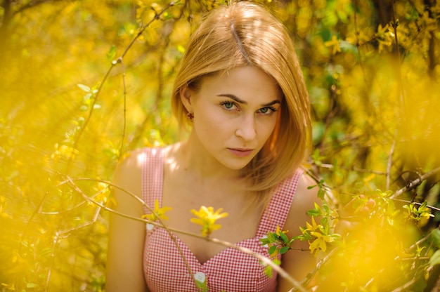 Retrato de una joven mujer rubia vestida con un vestido rosa de pie cerca del árbol floreciente amarillo