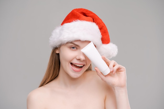 Retrato joven mujer sana y bien cuidada con sombrero de santa sosteniendo tubo blanco