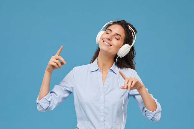 Retrato de joven mujer sonriente en auriculares escuchando música y disfrutándola contra el fondo azul.