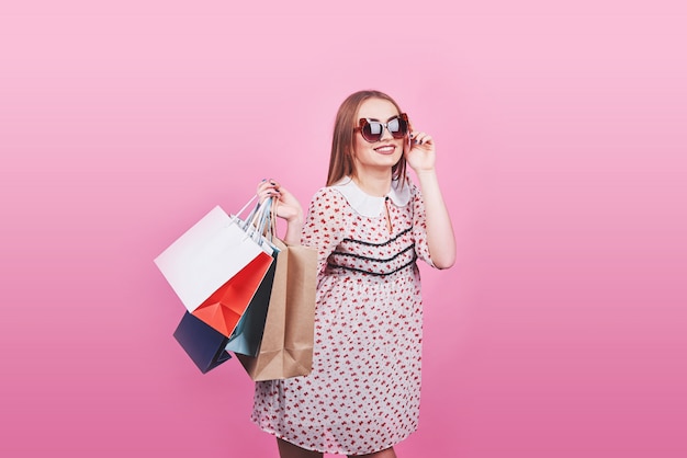 Retrato de joven mujer sonriente feliz con bolsas de compras en rosa