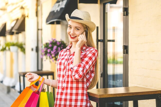 Retrato de joven mujer sonriente feliz con teléfono. Mujer joven con bolsas de compras. Concepto de compra en línea