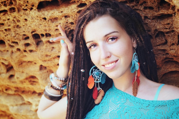 Retrato de una joven mujer sonriente con un peinado de rastas vestida con un vestido de encaje azul y aretes boho chic azules