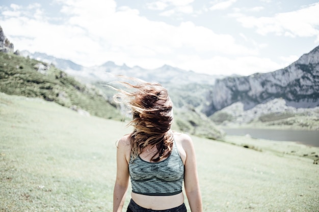 Retrato de joven mujer sonriente con el rostro parcialmente cubierto de pelo volador en un día ventoso de pie en la montaña - mujer despreocupada