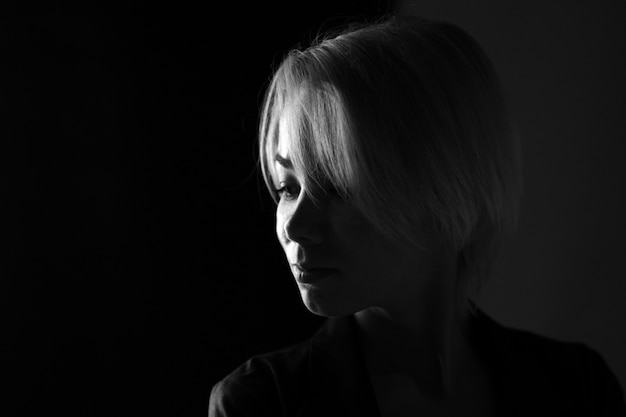 Retrato de una joven mujer triste de cerca mirando a otro lado, fotografía en blanco y negro oscuro