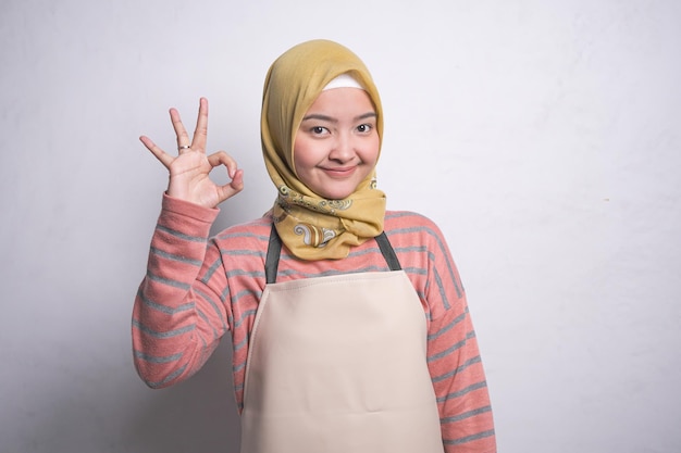 Retrato de una joven musulmana asiática sonriente de unos 20 años usando hiyab y delantal mientras muestra un gesto bien aislado sobre fondo blanco Concepto de estilo de vida musulmán de ama de casa de personas