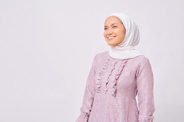Retrato de una joven musulmana asiática sonriente mirando el espacio de la copia y sintiéndose confiada aislada sobre el fondo blanco