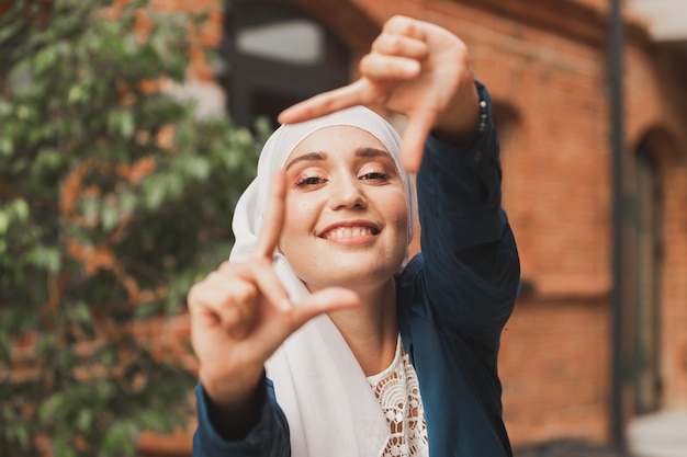 Foto retrato de joven musulmana haciendo un marco de cámara con los dedos al aire libre