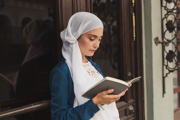 Retrato de joven musulmana con hijab libro de lectura al aire libre