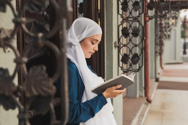 Retrato de joven musulmana con hijab libro de lectura al aire libre