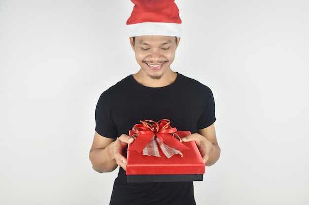 Retrato, de, joven, en, navidad, sombrero, sonriente, tenencia, caja de regalo roja, en, fondo gris