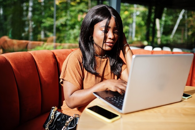 Retrato de una joven negra de belleza, vestida de naranja, sentada con una laptop en la oficina.