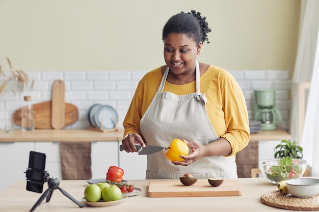 Retrato de una joven negra cocinando una comida saludable en la cocina y grabando un espacio de copia de video