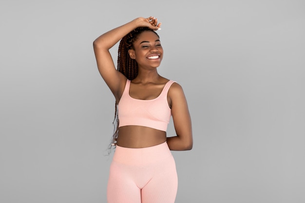 Retrato de una joven negra feliz con ropa deportiva posando y sonriendo en un estudio gris