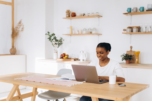 Retrato de una joven negra sentada en la cocina y trabajando en una laptop desde casa