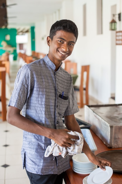 Retrato de un joven negro camarero frotando platos en un restaurante en Sri Lanka